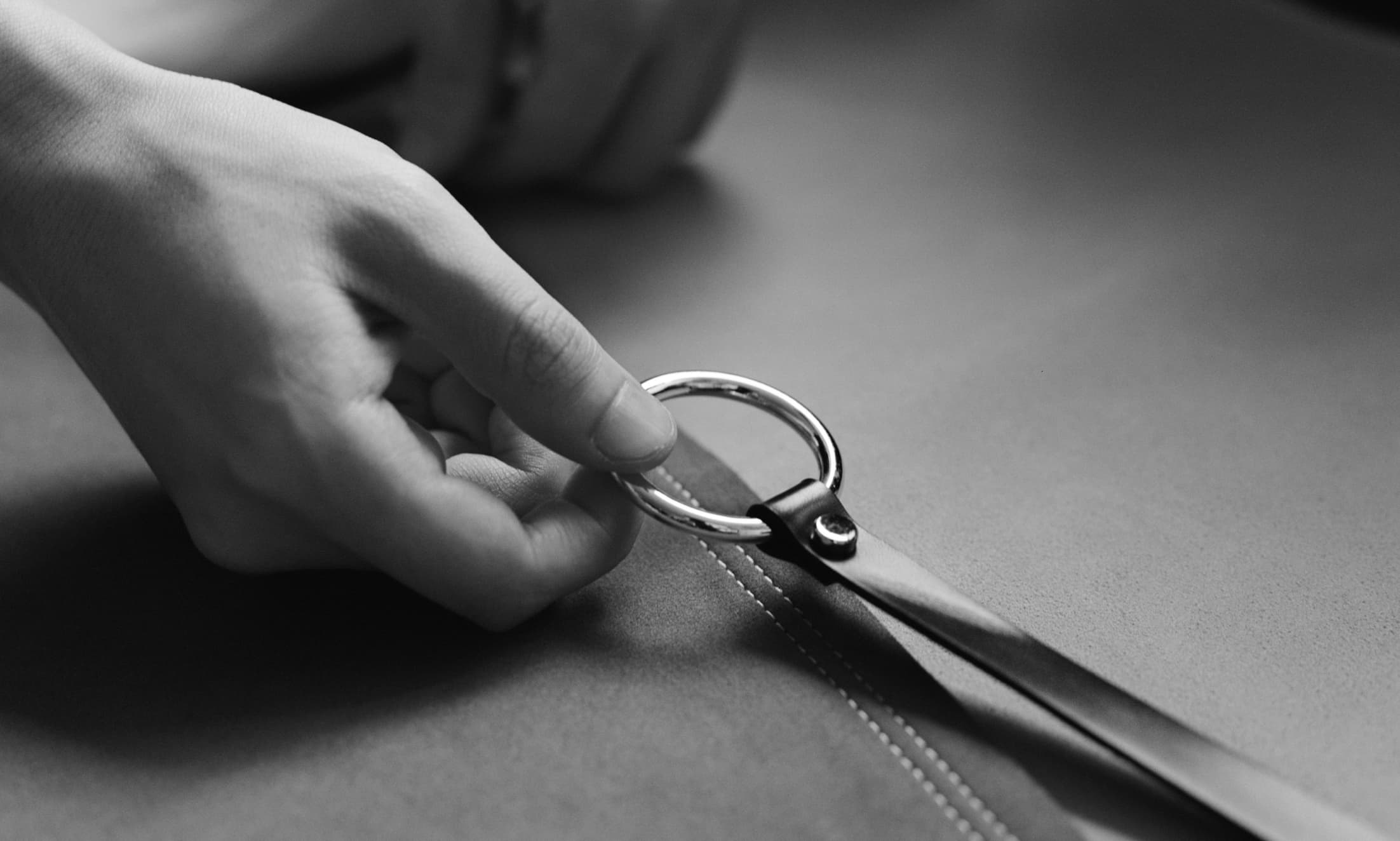 A monochromatic photo of a leather craftsman pulling a silver tab across seams.